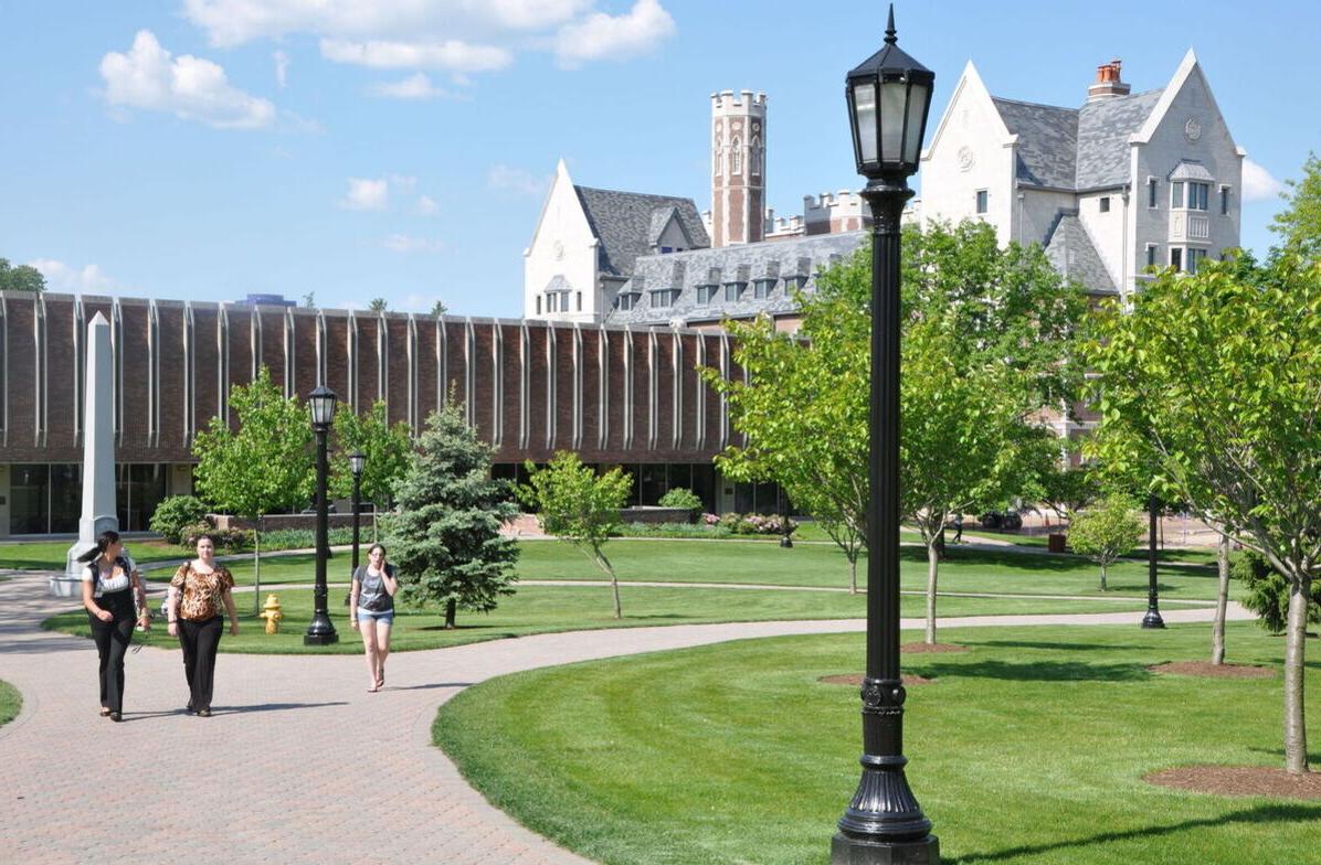 Students walk across campus with the Gannett-Tripp Library and Meier Hall in the background