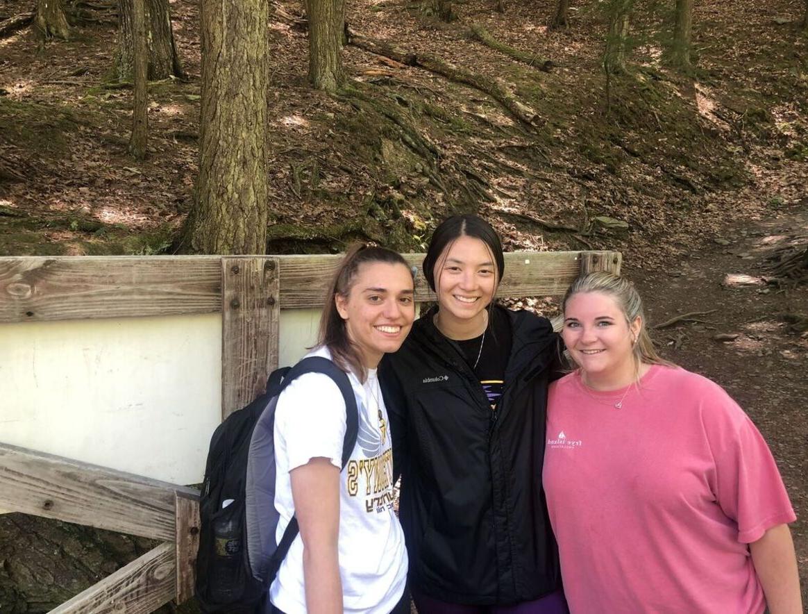 Three female students stand along a nature trail